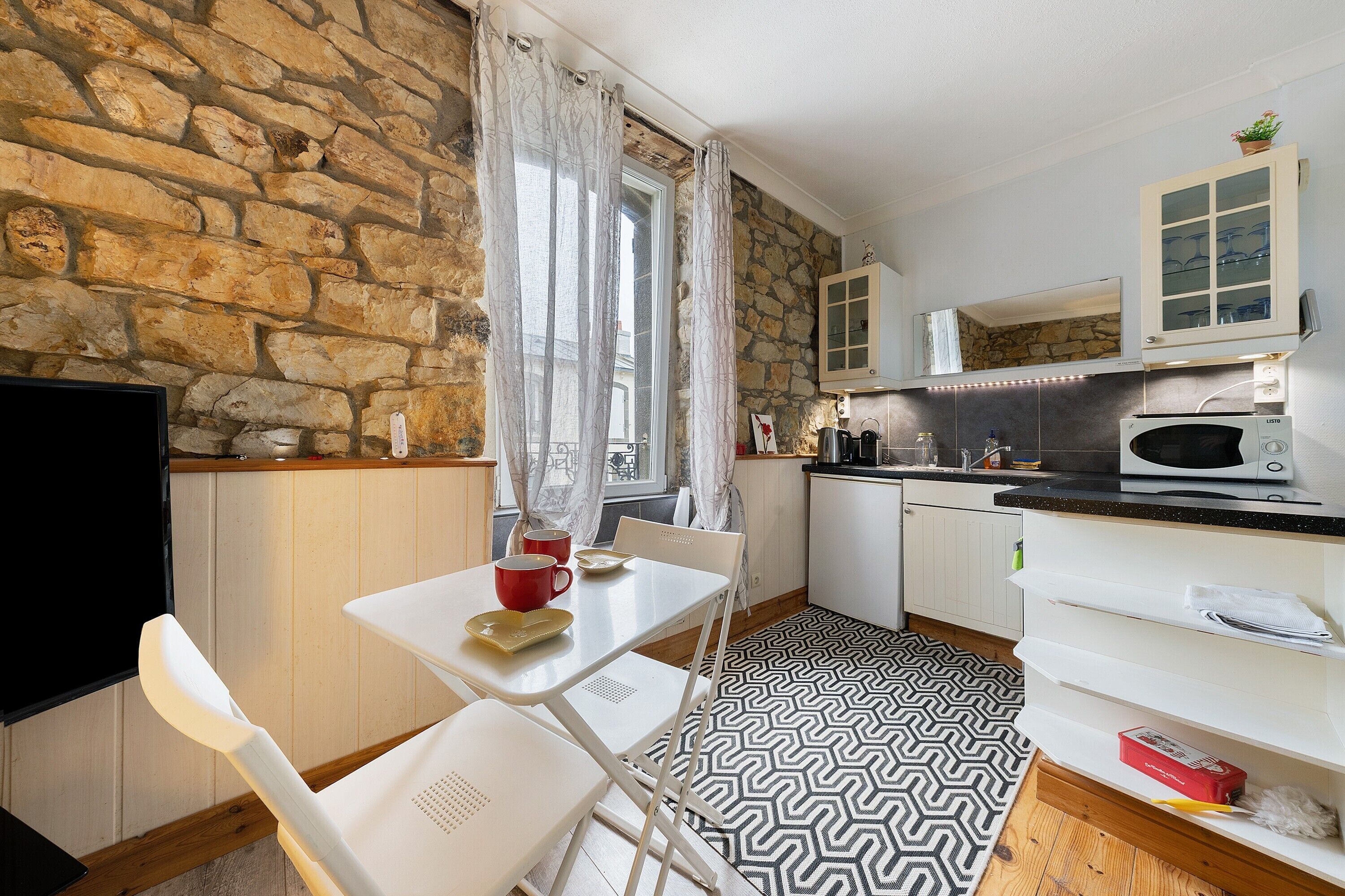Une cuisine compacte avec un mur en pierre, un four à micro-ondes, un évier et un coin repas comprenant une table et des chaises.