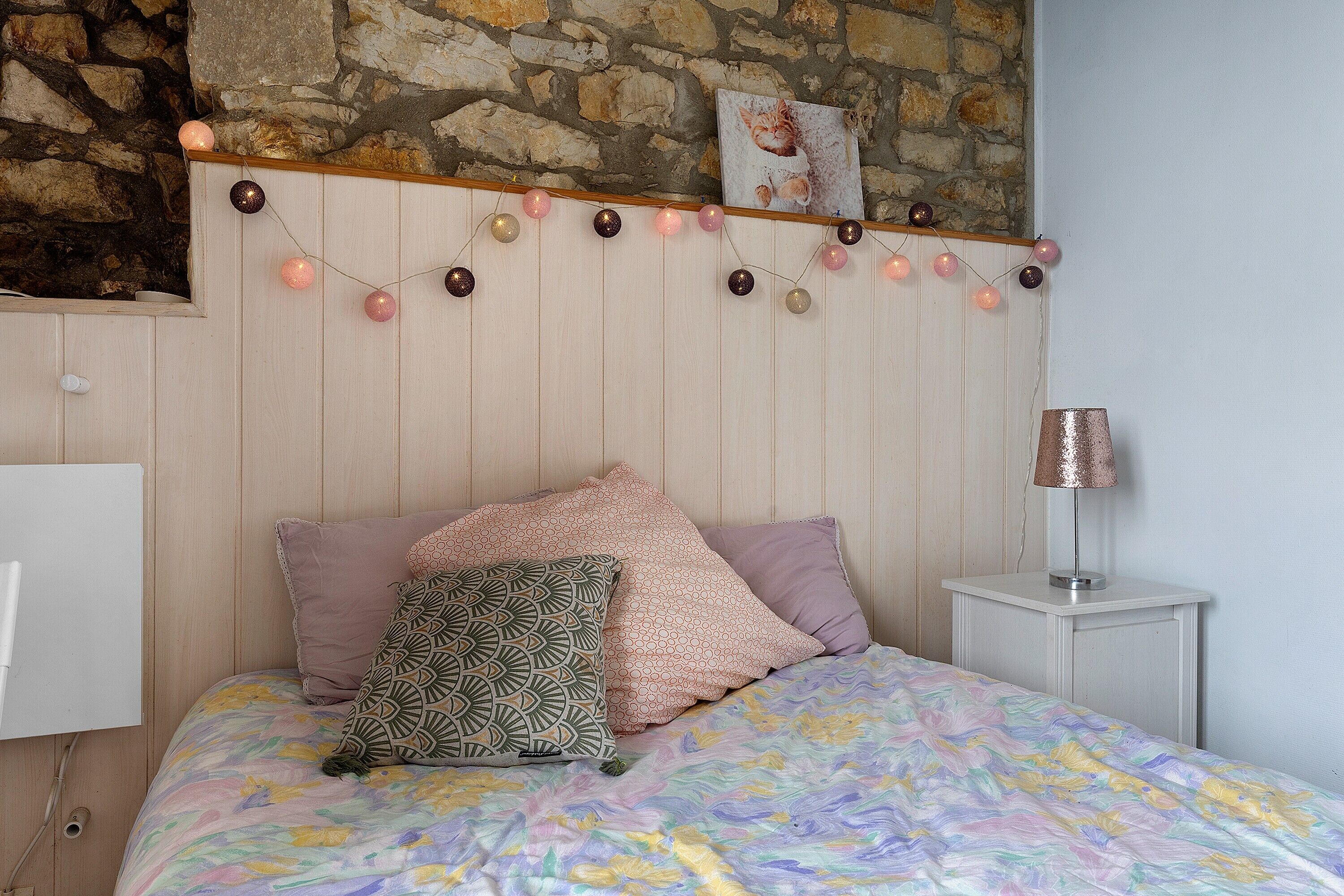 A bedroom with a bed, pillows, a lamp, and a string of lights.