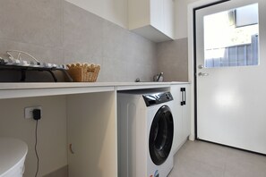 Ein Waschbereich mit Waschmaschine, Wäschekorb und Regal mit gestreiftem Gegenstand.