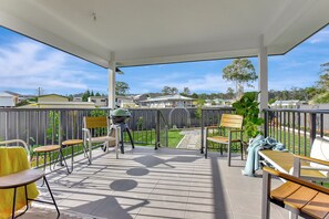 Eine überdachte Terrasse mit Grill, Gartenmöbeln und Blick auf eine Wohngegend.