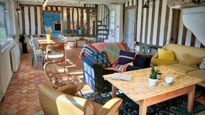 A rustic interior with a dining area, sofa, and a staircase leading to a kitchen. - The House Across the Street • Family-Friendly Vacation Rental • Normandy - Calvados (Saint-Philbert-des-Champs)