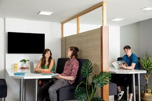 A modern office space with three individuals seated at a table, a large flat-screen TV on the wall, and potted plants. - Student Only - Ty Pont Haearn - Cardiff (Cardiff)