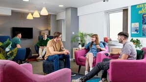 A group of people sitting on colorful chairs in a modern room with pendant lights, a flat-screen TV, and a bulletin board with notices. - Student Only - Ty Pont Haearn - Cardiff (Cardiff)