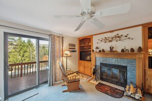 Ein Wohnzimmer mit Kamin, Deckenventilator, Fernseher und einer Schiebetür zu einer Terrasse.