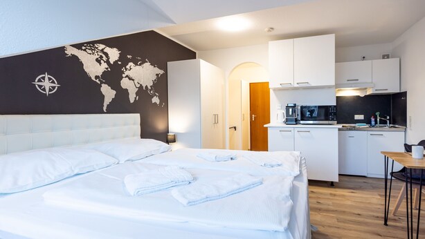 Ett hotellrum med en säng, ett litet kök, en matplats och en världskarta på väggen.