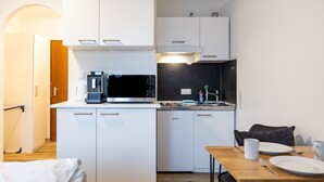 Ett kompakt kök med vita skåp, en mikrovågsugn, en kaffebryggare och en matplats med ett bord och stolar.