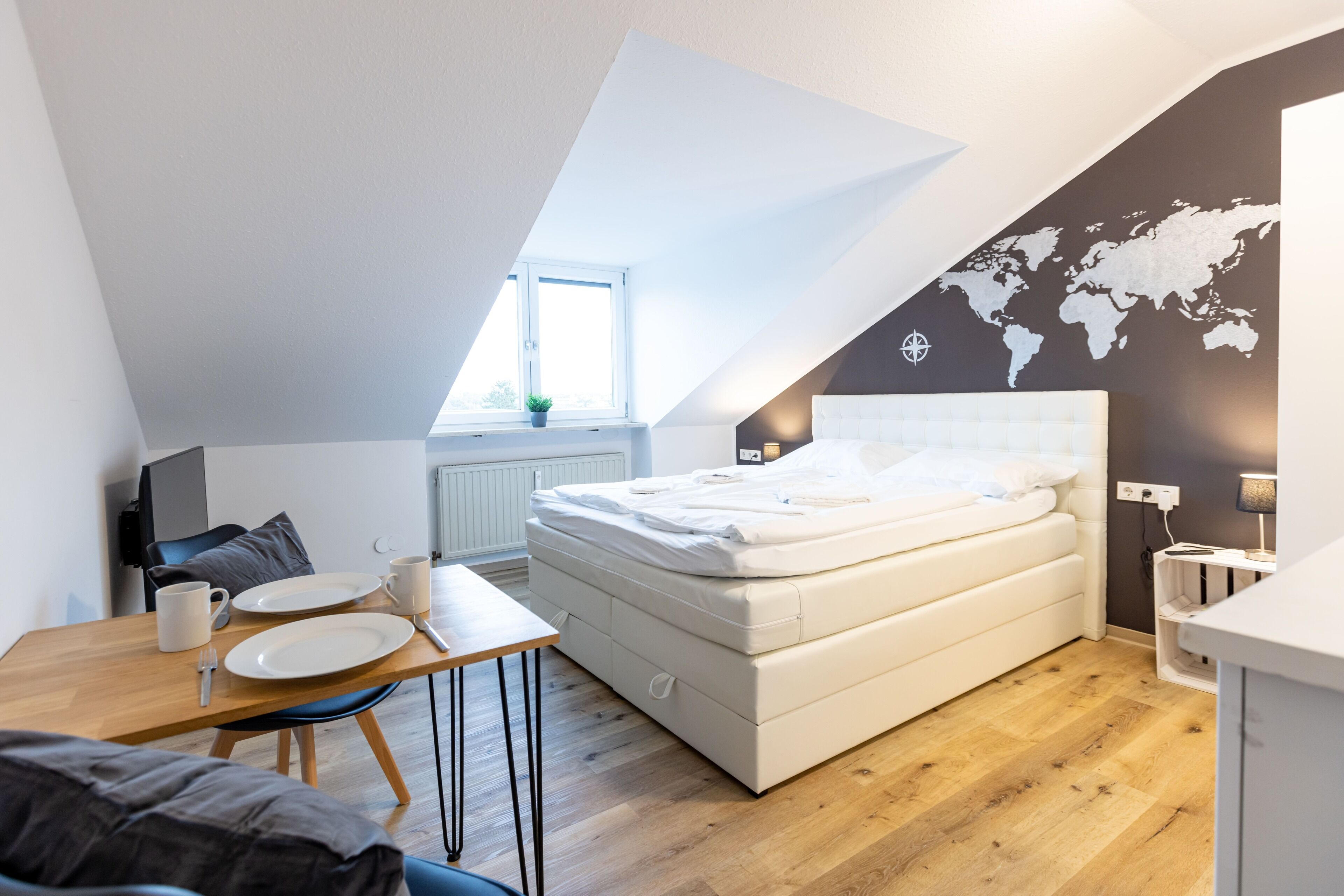 Un dormitorio moderno con techo estilo loft, una cama, una mesa de comedor y un mapa del mundo en la pared.