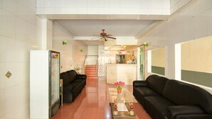 A hotel lobby with two black leather sofas, a glass coffee table, a refrigerator, and a reception desk. - Cozy Double Escape W/ Free Wifi and Parking (Makassar)