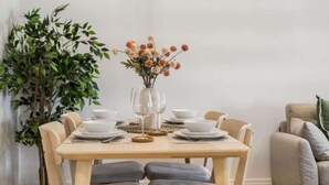 A dining table set with white plates, bowls, and glasses, surrounded by chairs. - Stylish 2BR Marlow Stay + Parking - By Tempstay (Marlow)