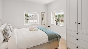 A bedroom with a bed, two windows, a wardrobe, and a view of the outside. - Stylish 2BR Marlow Stay + Parking - By Tempstay (Marlow)