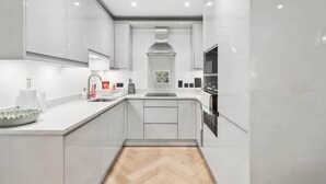 A modern kitchen with white cabinetry, a herringbone floor, and a built-in oven. - Stylish 2BR Marlow Stay + Parking - By Tempstay (Marlow)
