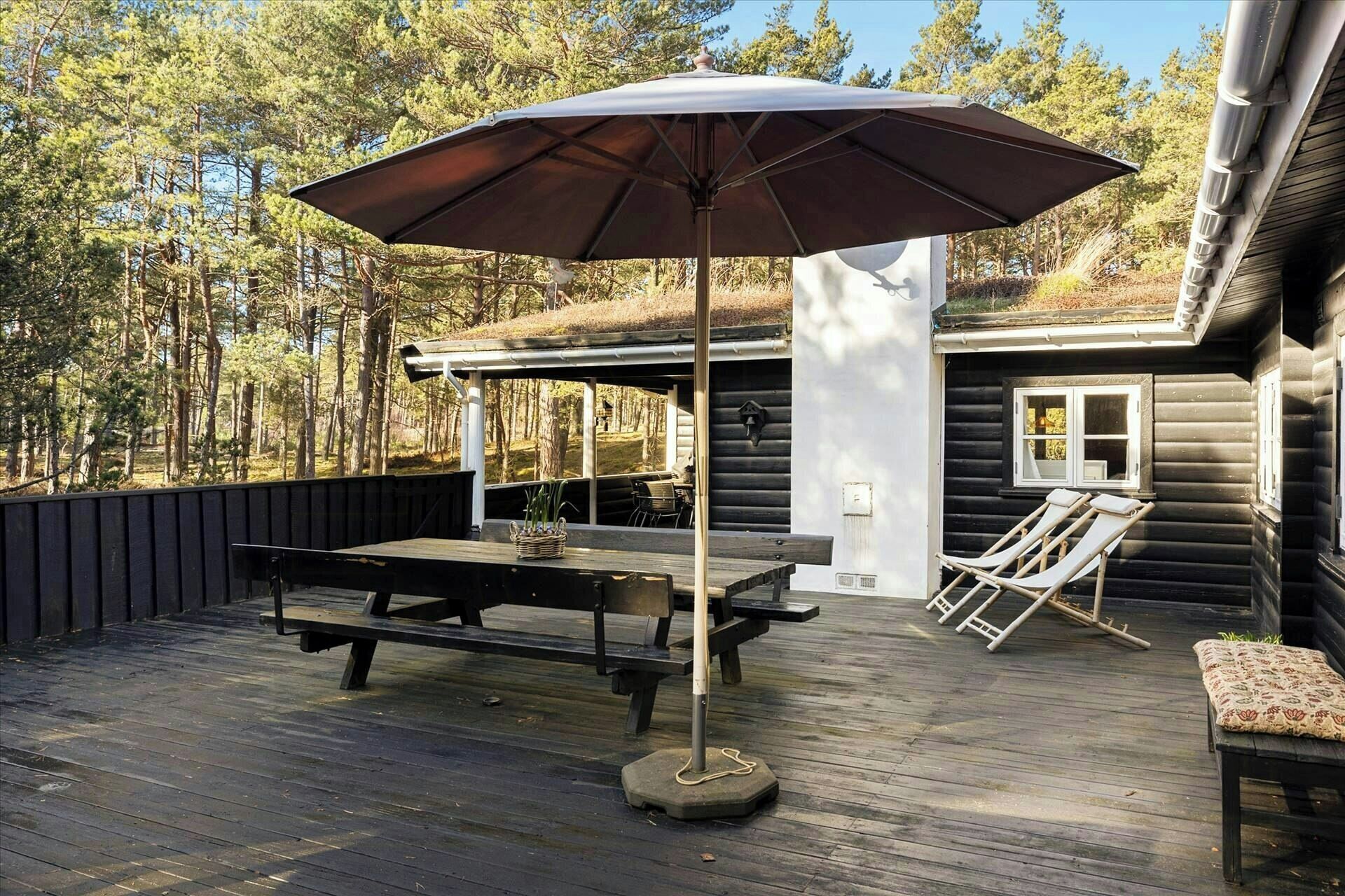 A wooden deck with a table and chairs, an umbrella, and a building with a window and a door.