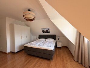 A bedroom with a bed, wardrobe, bedside table, and a ceiling light fixture. - Blauer Peter Luxury Vacation Home with Fireplace and Sauna on Usedom (Zempin)