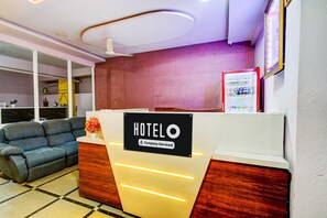 A hotel reception desk with a sign indicating it's company-serviced, a sofa, and a refrigerator stocked with beverages. - Hotel O Hafizpet Railway Station (Hyderabad)