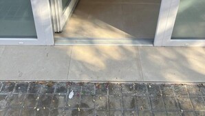 Une porte vitrée donne accès à une pièce dont le sol est recouvert de carreaux et où se trouve un paillasson.