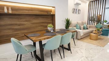 Un salon moderne avec un coin repas, comprenant une table à manger en bois, des chaises bleu clair, un canapé beige et une plante décorative.