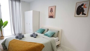 Ein Schlafzimmer mit Bett, Kissen, Decke, Kleiderschrank, einem Gemälde und einer Pflanze.