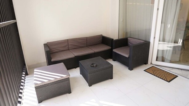 Ein Balkon mit einer Sitzecke, zwei Poufs und einer Glastür.