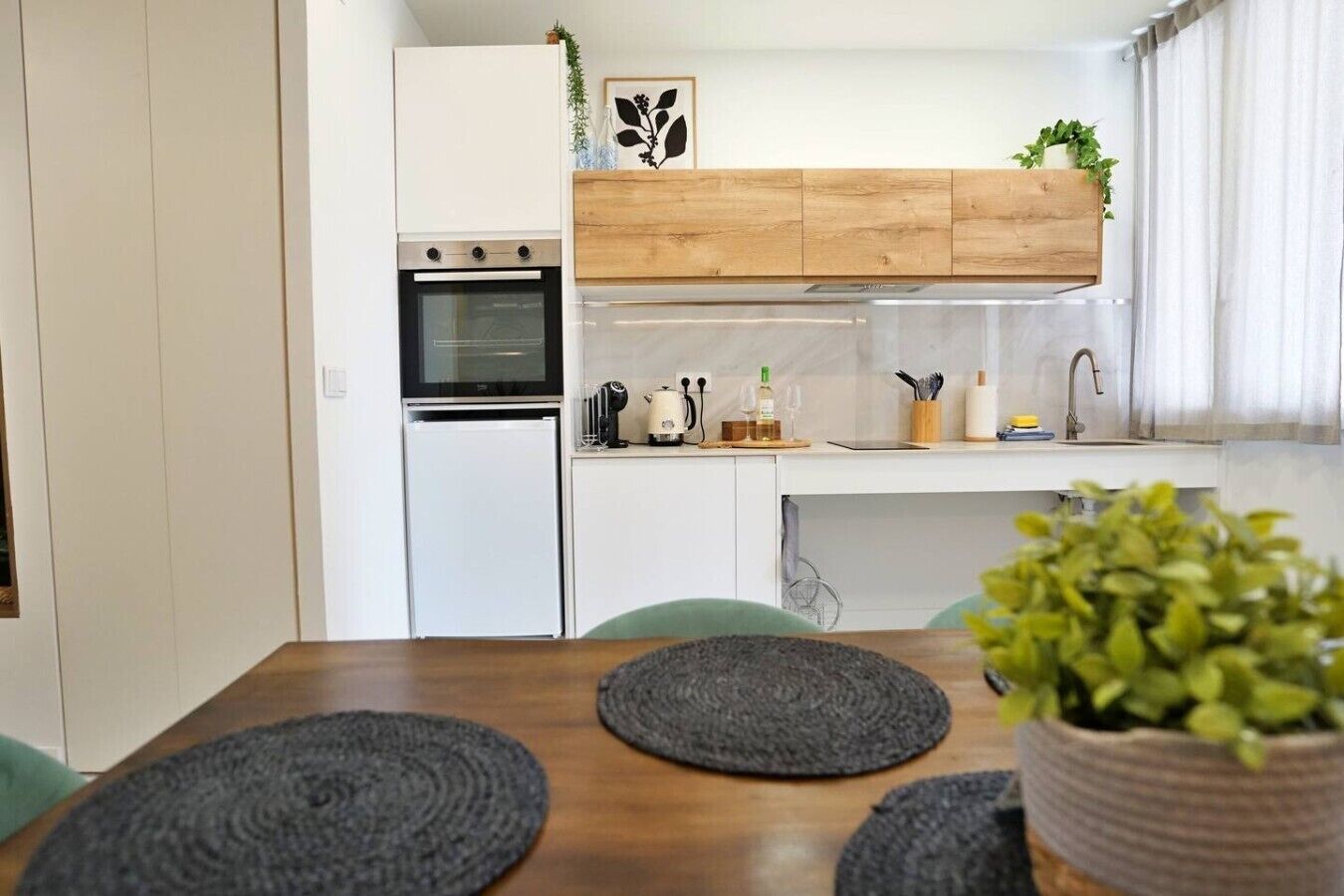 A modern kitchen with white cabinetry, a built-in oven, and a wooden upper shelf.