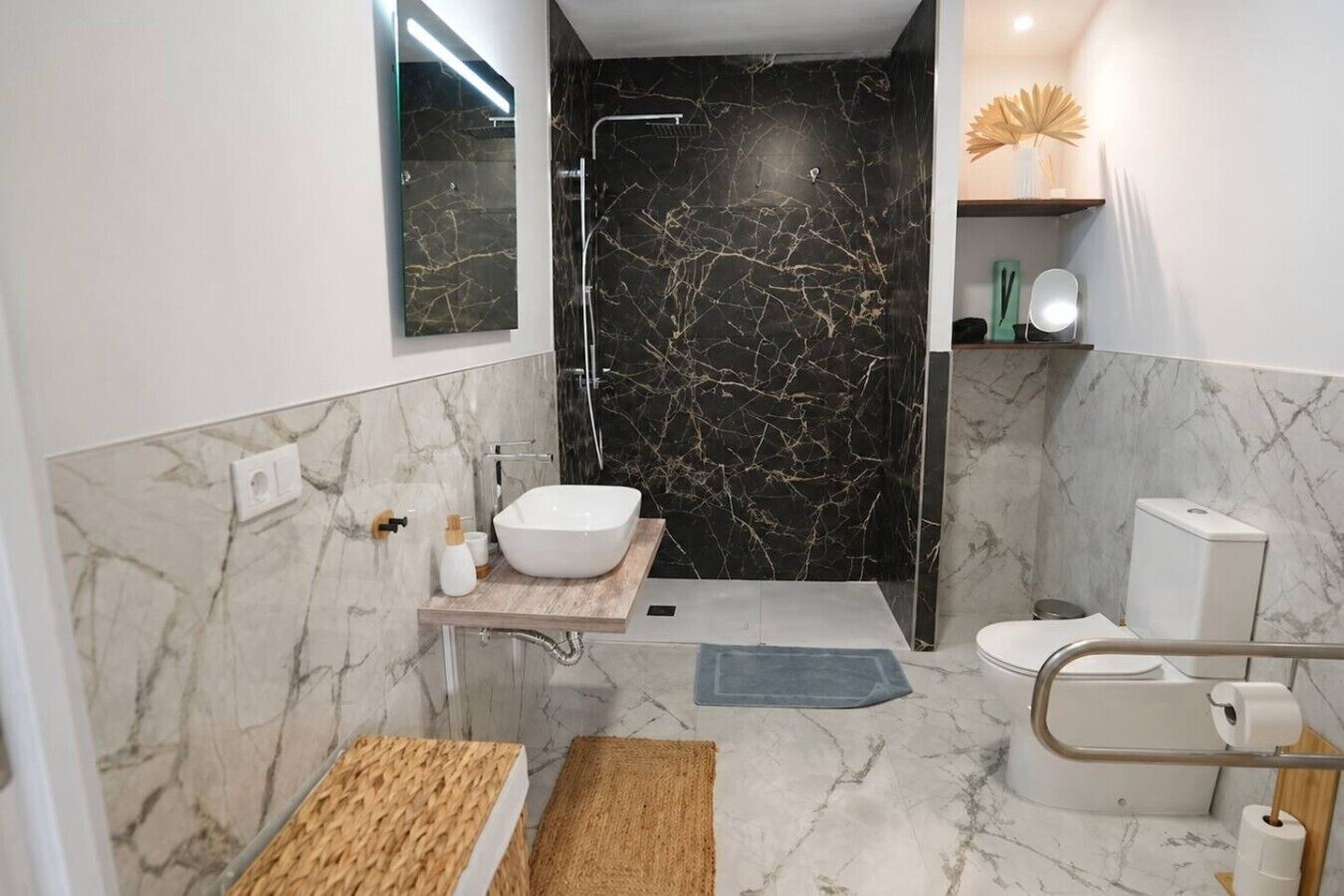 Een moderne badkamer met een wit wastafelmeubel, zwarte marmeren wanden, een douche en een toilet.