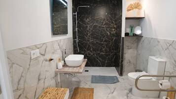 Een moderne badkamer met een wit wastafelmeubel, zwarte marmeren wanden, een douche en een toilet.