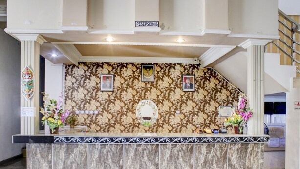 A reception desk with a floral patterned backdrop, a sign above it, and a staircase to the right. - Nascar Family Cozy Twin Stay (Palangkaraya)