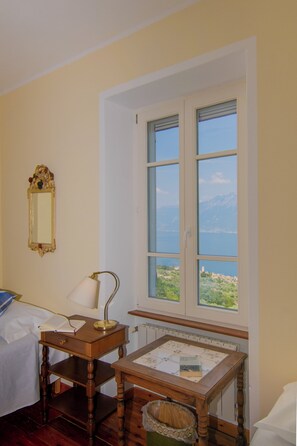 Une chambre avec un lit, une table de chevet avec une lampe, une petite table avec un livre, une fenêtre donnant sur les montagnes et un miroir au mur.