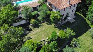 Ovenfra-billede af en ejendom med swimmingpool, en bygning i sten med rødt tegltag og frodig beplantning.