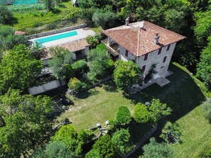 Eine Vogelperspektive auf ein Anwesen mit Swimmingpool, ein Steinhaus mit rotem Ziegeldach und üppiger Vegetation.