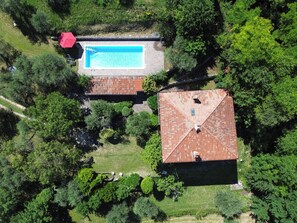 An aerial view of a property with a swimming pool, a red-roofed building, and surrounding greenery. - Villa Supina | Panoramic Pool, Private Garden & Lake Garda Views (Lombardia)