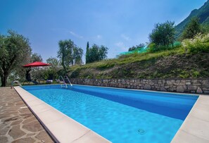 A rectangular swimming pool with a stone border and a stone wall on one side. - Villa Supina | Panoramic Pool, Private Garden & Lake Garda Views (Lombardia)