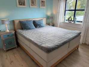 A bedroom with a bed, two bedside tables, a window with curtains, and a view of the outside.