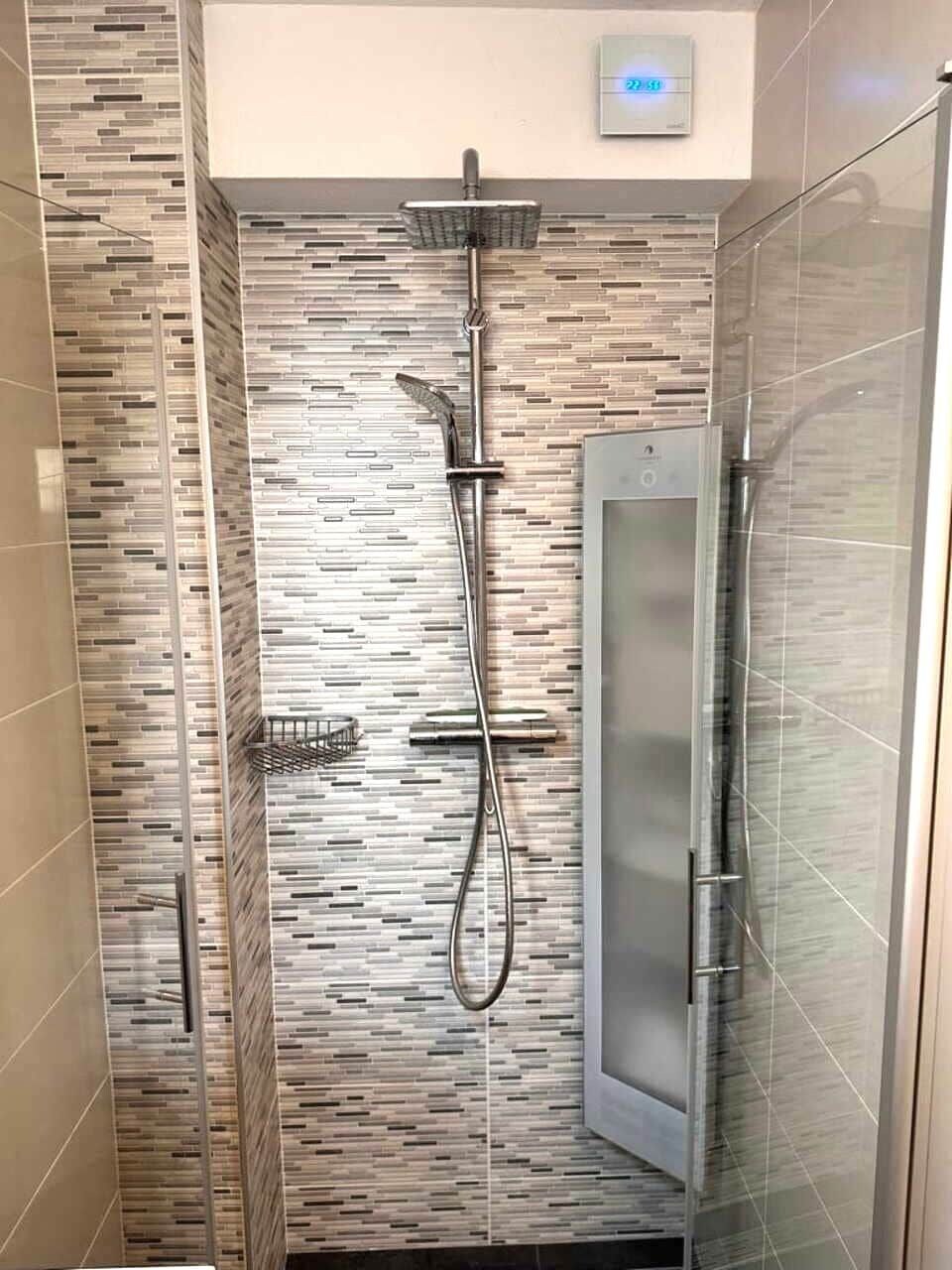 Une douche moderne dotée d’un écran numérique, d’une porte en verre et d’un mur carrelé.