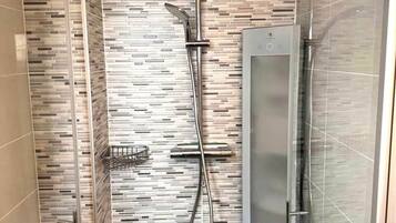 Une douche moderne dotée d’un écran numérique, d’une porte en verre et d’un mur carrelé.
