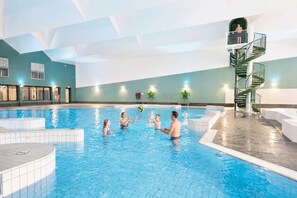 An indoor swimming pool with a family playing, a staircase, and a view of the sky.