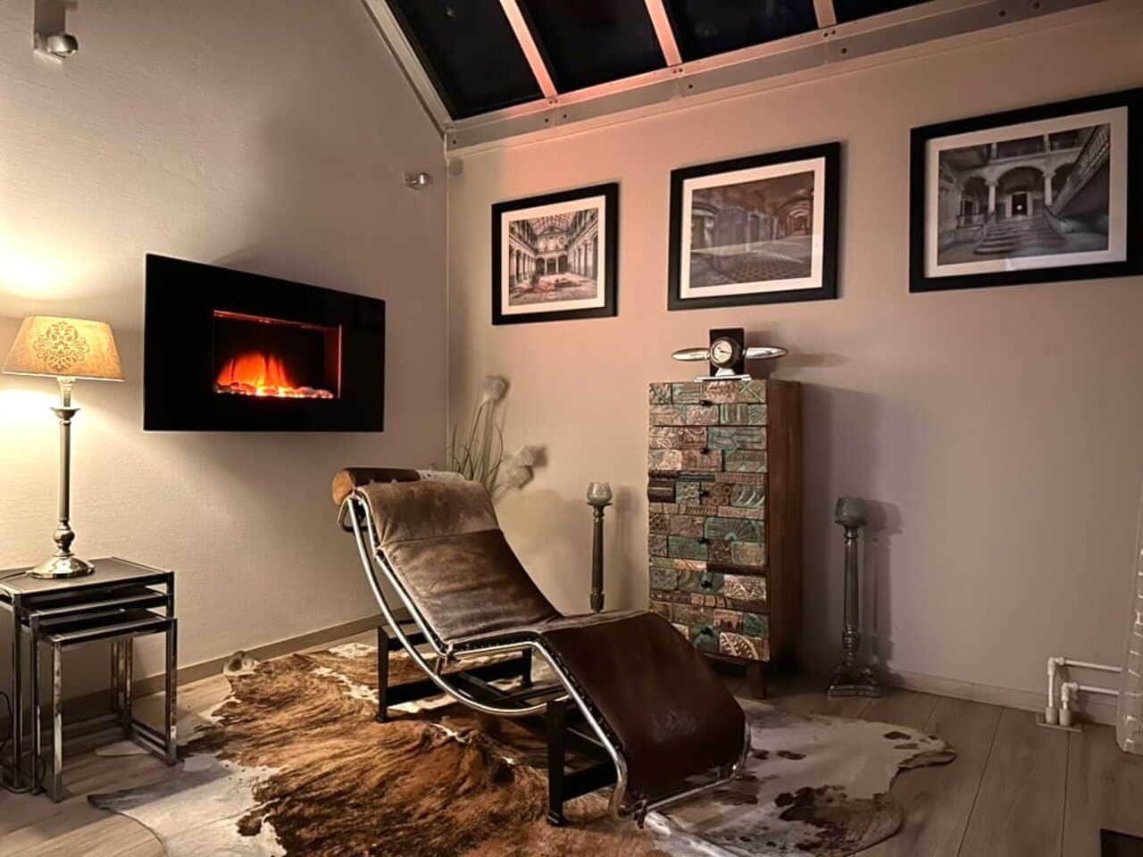 A room with a reclining chair, a fireplace, framed pictures on the wall, and a patterned rug.