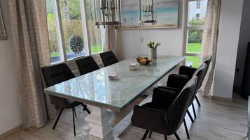 A dining room with a large glass table, black chairs, a chandelier, and a view of the outdoors.