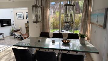 Un coin repas avec une table en verre, des chaises noires, un vase de fleurs et une vue sur un jardin grâce à de grandes fenêtres.