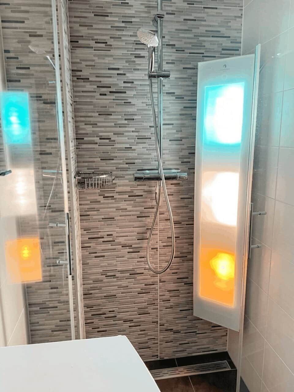 Une salle de bain moderne avec une douche, une paroi en verre et un luminaire fixé au mur.