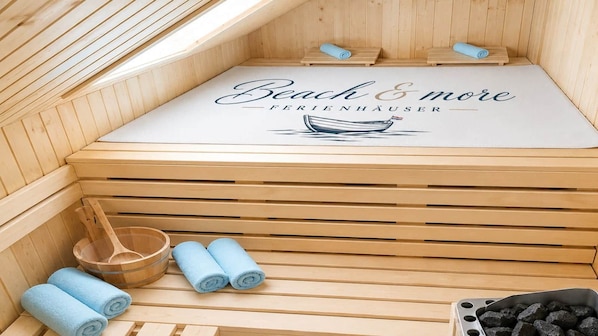A sauna with wooden slats, a bench, a wooden bucket, and rolled towels.