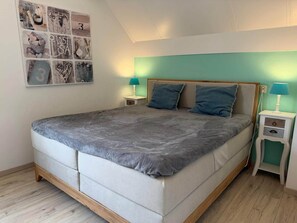 A bedroom with a large bed, two bedside tables, a wall with a collage, and a sloped ceiling.