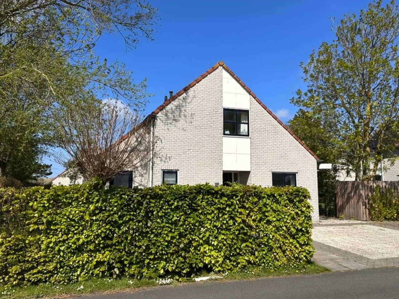 A modern two-story house with a brick exterior, a white window, and a well-maintained hedge in front.