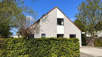 A modern two-story house with a brick exterior, a white window, and a well-maintained hedge in front.