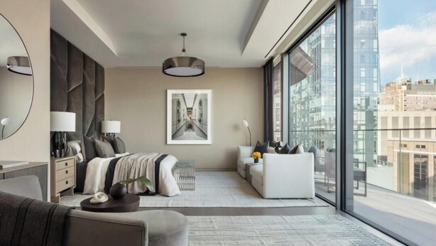 A modern bedroom with a large bed, a sofa, a desk, and a large window offering a city view.