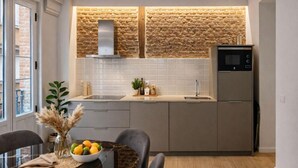 Uma cozinha moderna com painel de parede de pedra, forno embutido e área de jantar com mesa e cadeiras de vidro.