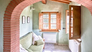 Um quarto com um arco de tijolos, uma porta de madeira, um radiador e uma janela com persianas de madeira.