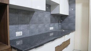 Una cocina con baldosas grises, encimera negra y armarios blancos.