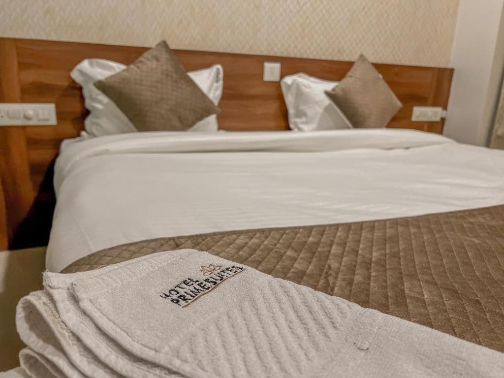 Une chambre d’hôtel avec un lit bien fait, une tête de lit et une couverture visible portant le logo de l’hôtel.