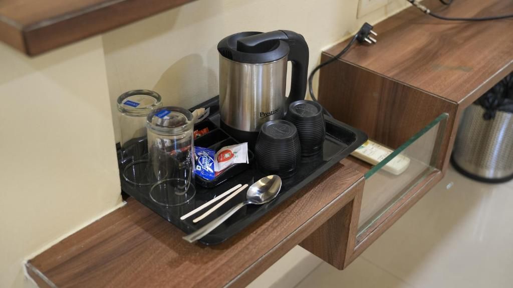 A tray with a coffee maker, cups, a glass, a spoon, and condiments.