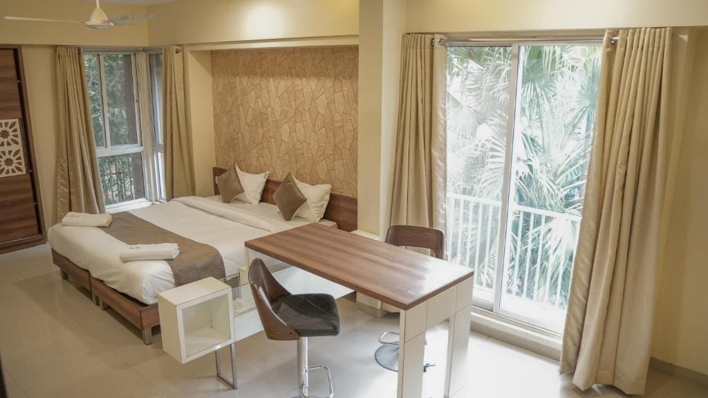 Habitación de hotel con cama, escritorio y silla. Tiene una ventana con cortinas y un ventilador de techo.